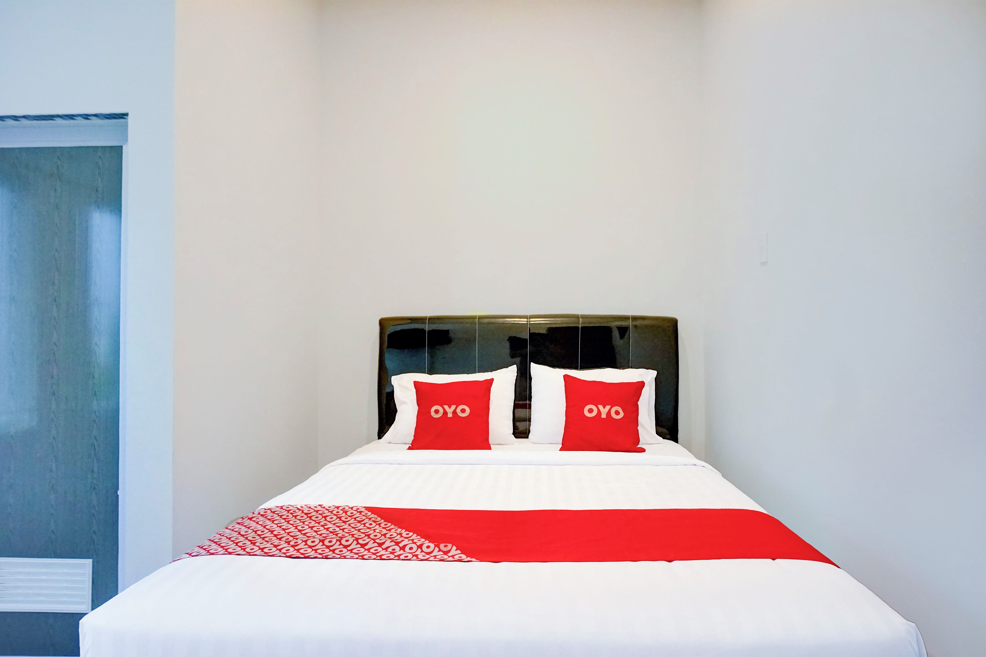 Una cama bien hecha con ropa de cama blanca y roja, dos almohadas con el texto 'OYO' y una manta de diseño rojo y blanco.