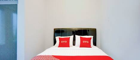 Una cama bien hecha con ropa de cama blanca y roja, dos almohadas con el texto 'OYO' y una manta de diseño rojo y blanco.