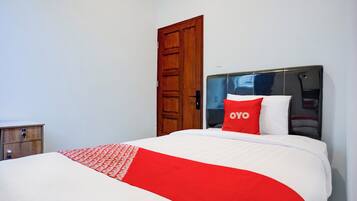 A neatly made bed with a red and white bedspread, a wooden nightstand, and a wooden door.