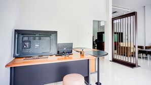 Un comptoir d’accueil avec un ordinateur, un téléphone et une petite table. Il y a une chaise devant le comptoir et un paravent en bois à l’arrière-plan.