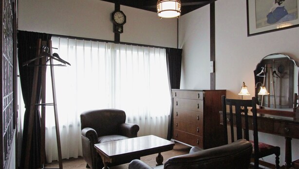Une pièce comprenant une table en bois, un fauteuil en cuir, une armoire en bois, une horloge au mur et un luminaire suspendu.