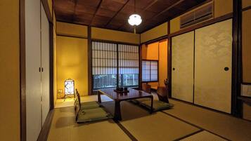 A traditional Japanese room with tatami flooring, a low table, sliding doors, and a view through a shoji screen.