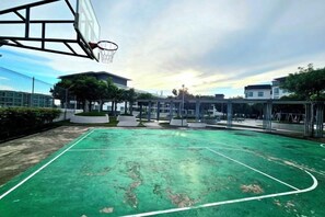 Ein Basketballplatz im Freien mit grüner Spielfläche, umgeben von Gebäuden und Bäumen.
