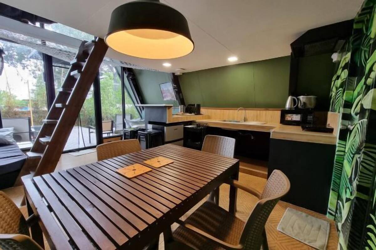 A modern room with a wooden table, chairs, a kitchen area, and a large window.