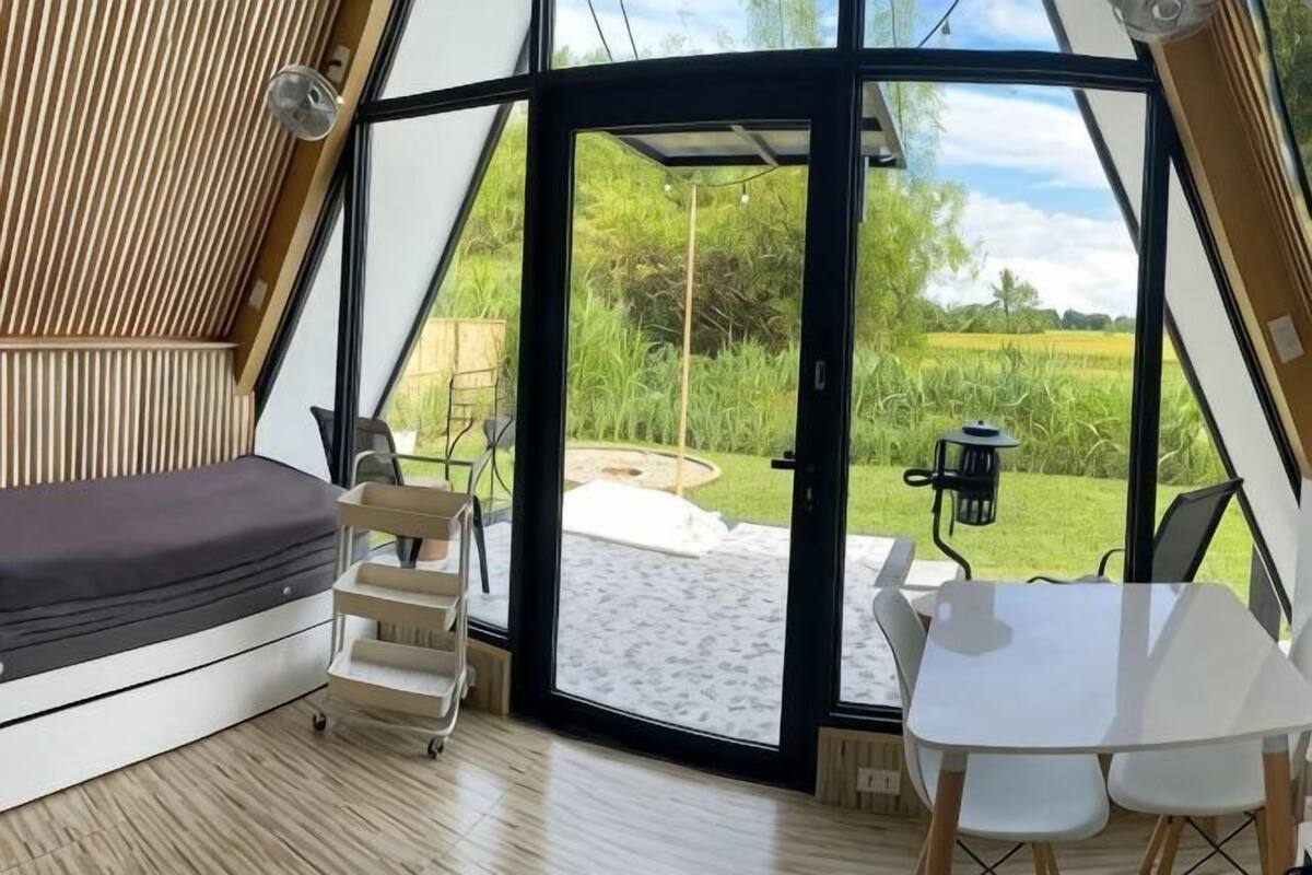 A tent-style accommodation with a bed, a table, and chairs, and a view of a grassy outdoor area.