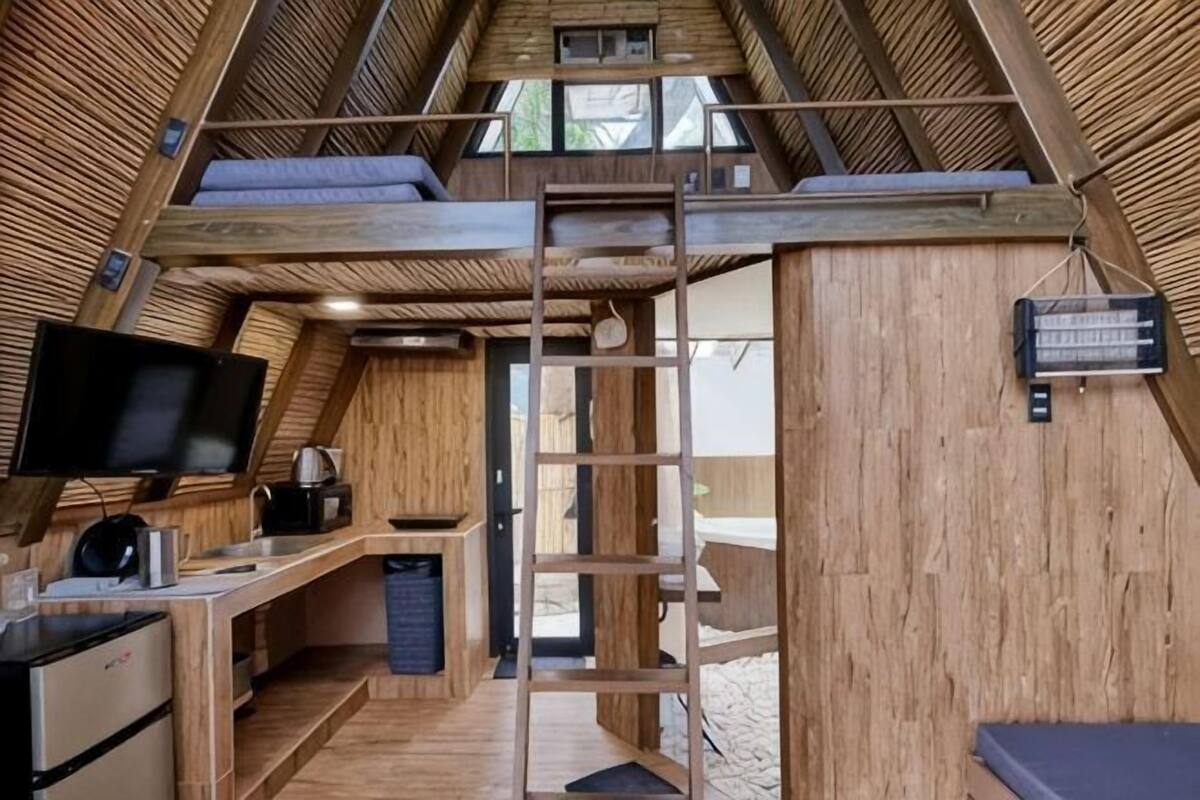 A loft-style room with a wooden interior, a desk with a computer, a TV, and a ladder.