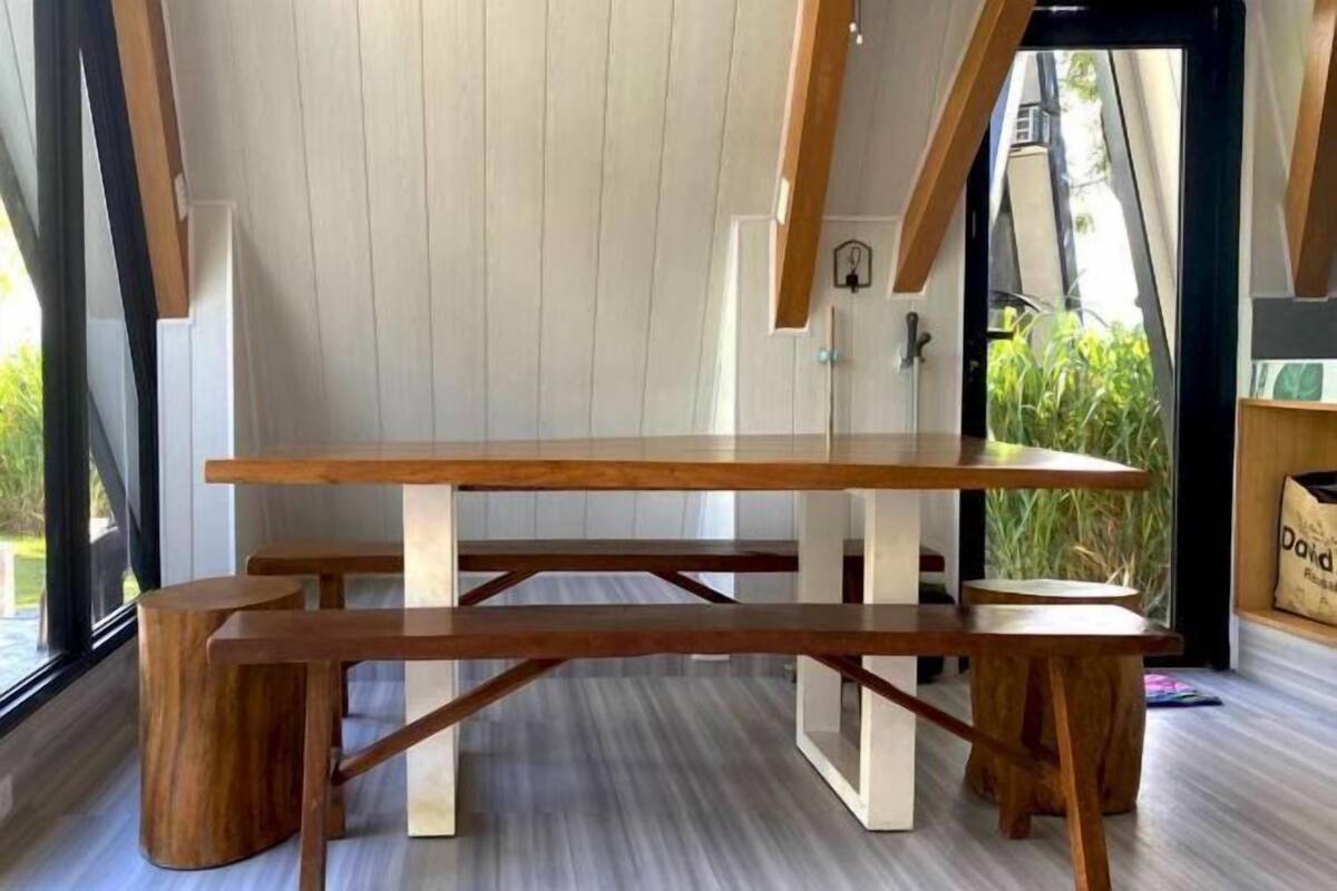 A dining area with a wooden table and benches, white walls, and a view of greenery outside.