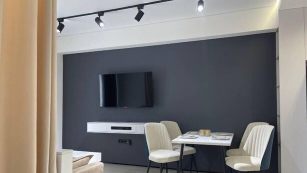 Una zona menjador moderna amb un televisor de pantalla plana fixat a una paret fosca, una taula de dinar blanca i quatre cadires.