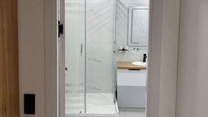 Un bany modern amb una cabina de dutxa de vidre, un moble de tocador de fusta i un respatller de marbre.
