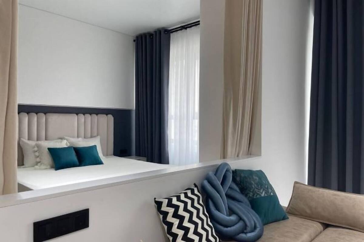 A modern hotel room with a bed, a sofa, and a window with curtains.