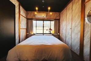 A room with a large bed, wooden walls, a chandelier, and a window with curtains. - Rakuyado kyotofushimi II (Kyoto)