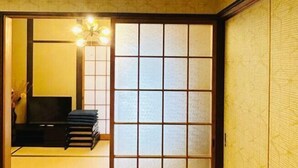 A traditional Japanese room with tatami flooring, a shoji screen door, a television, and a stack of books.