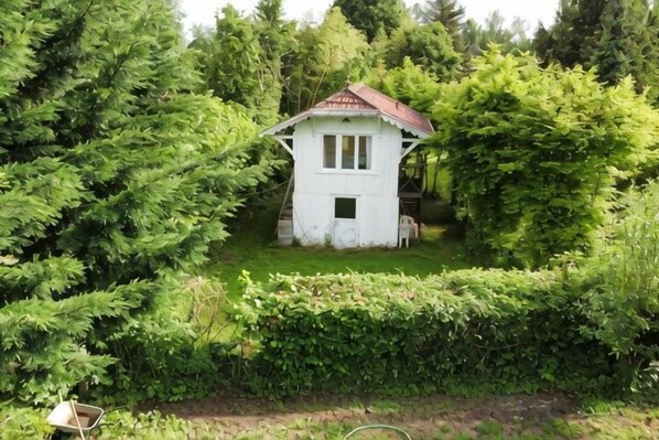 Un pequeño edificio blanco con techo rojo rodeado de abundante follaje verde.