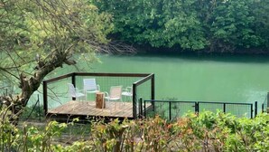 A wooden deck with chairs and a table, surrounded by a fence, overlooking a body of water.