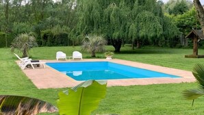 A rectangular swimming pool with a tiled deck, surrounded by grass and trees.