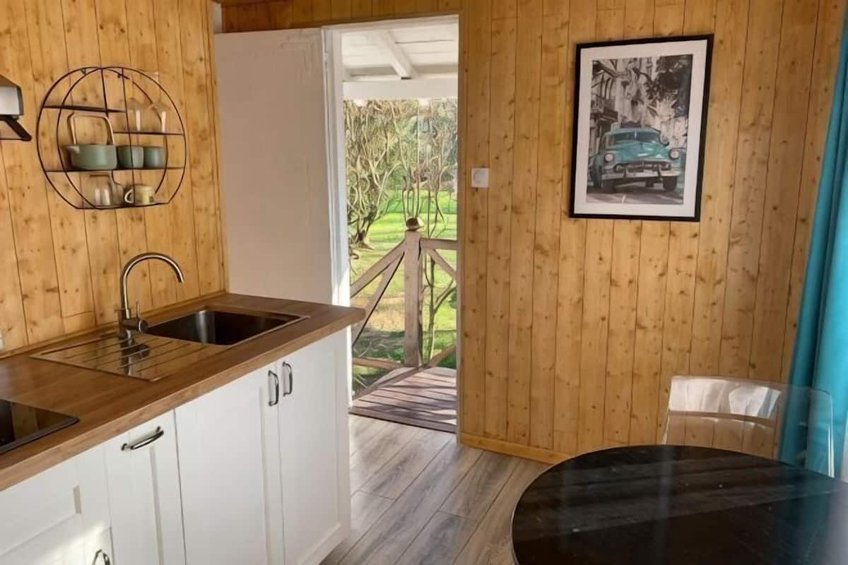 A wooden interior with a kitchen area, a dining table, and a door leading outside.
