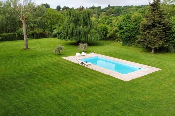 A rectangular swimming pool with a tiled edge, surrounded by a well-maintained lawn, and trees in the background. - Romantic Nature Chalet – Peaceful Escape by the Marne River (Isles-les-Villenoy)