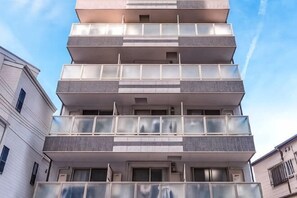Un edificio de varios pisos con balcones, cielo despejado y edificios colindantes.