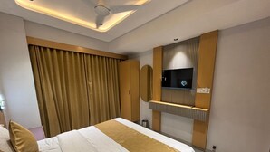 A hotel room with a large bed, a flat-screen TV mounted on the wall, and a large window with curtains. - Hotel Prenix Sky- Gota (Ahmedabad)
