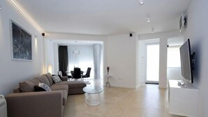 A modern living room with a sofa, a coffee table, and a flat-screen TV. There is a dining area in the background with a table and chairs. - Luxury Apartment Split with pool (Split)