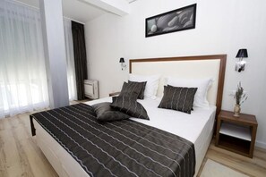 A hotel room with a large bed, bedside tables, a nightstand, a wall-mounted lamp, and a framed picture. - Luxury Apartment Split with pool (Split)