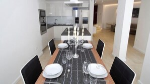 A modern dining area with a long table set for four, black chairs, and a kitchen in the background. - Luxury Apartment Split with pool (Split)
