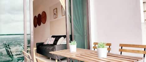 A balcony with a wooden table and chairs, a sofa, and a potted plant.