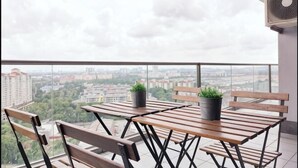 Un balcon avec une table et des chaises en bois, deux plantes en pot et une vue sur la ville.