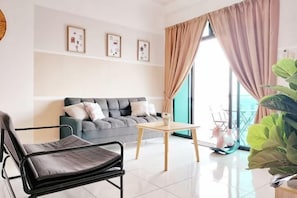 A modern living room with a grey sofa, a black chair, a small table, and a large plant. - Delight Homestay The Platino (Tebrau)