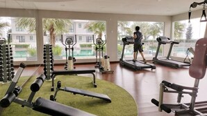 Une salle de sport équipée de tapis de course, d’appareils de musculation et d’un espace recouvert d’une moquette verte.