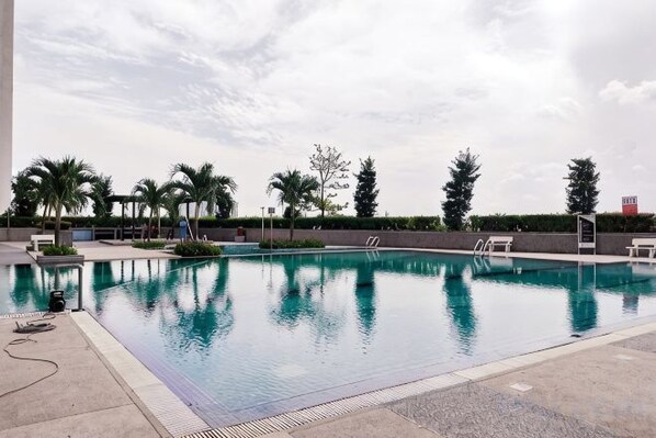 Una piscina con superficie de agua azul cristalina, rodeada de palmeras y una zona de terraza pavimentada.