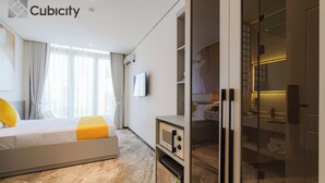A modern hotel room with a bed, a built-in microwave, a mini-fridge, and a glass-enclosed bathroom. - Cubicity Ton That Tung (Ho Chi Minh City)