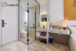 A modern bathroom with a glass-enclosed shower, a white sink, and a bedside table with a lamp. - Cubicity Ton That Tung (Ho Chi Minh City)
