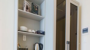 A compact kitchenette with a microwave, a small refrigerator, and a cabinet with shelves containing books and kitchenware. - Cubicity Ton That Tung (Ho Chi Minh City)