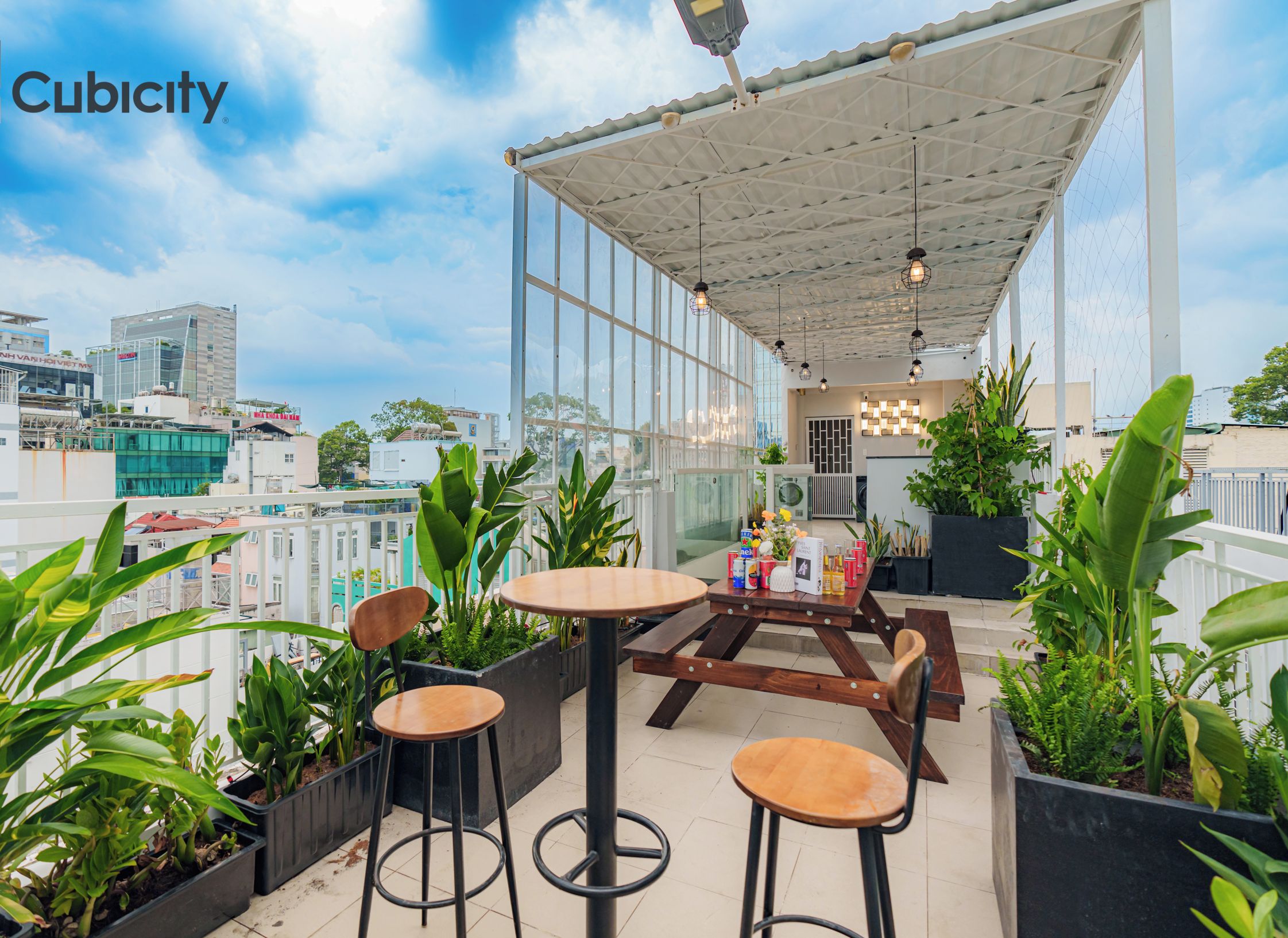 Una terraza en la azotea con zona de estar cubierta, plantas en macetas y vistas a la ciudad.