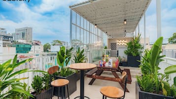 Una terraza en la azotea con zona de estar cubierta, plantas en macetas y vistas a la ciudad.