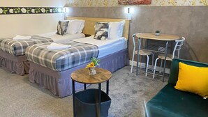A hotel room with two beds, a small round table with a vase, a trash bin, and a green couch. - Spacious First-Floor Super King or Twin Studio Apartment with Free Parking (Portsmouth)