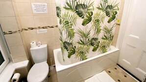 A bathroom with a toilet, sink, and shower curtain with a tropical leaf pattern. - Spacious First-Floor Super King or Twin Studio Apartment with Free Parking (Portsmouth)