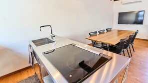 A modern kitchen with an induction cooktop, a built-in sink, and a dining area with a wooden table and chairs. - Kyobu Kiyomizu (Kyoto)