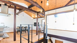 A modern interior with exposed wooden beams, a dining area with chairs, a kitchen area with a sink, and a large window providing natural light. - Kyobu Kiyomizu (Kyoto)