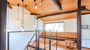 A modern interior with exposed wooden beams, a staircase, a seating area, and a kitchen with a microwave. - Kyobu Kiyomizu (Kyoto)