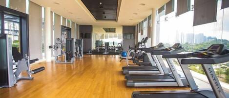 Uma academia com esteiras, equipamentos de exercício e amplas janelas com vista para a cidade.