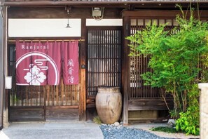 Ein traditionelles japanisches Gebäude mit einem hölzernen Eingang, einer großen Kübelpflanze und einem Schild mit japanischen Schriftzeichen.