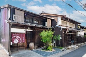 Un bâtiment japonais traditionnel, doté d’une façade en bois, d’un petit jardin et d’une enseigne indiquant la présence d’un restaurant.