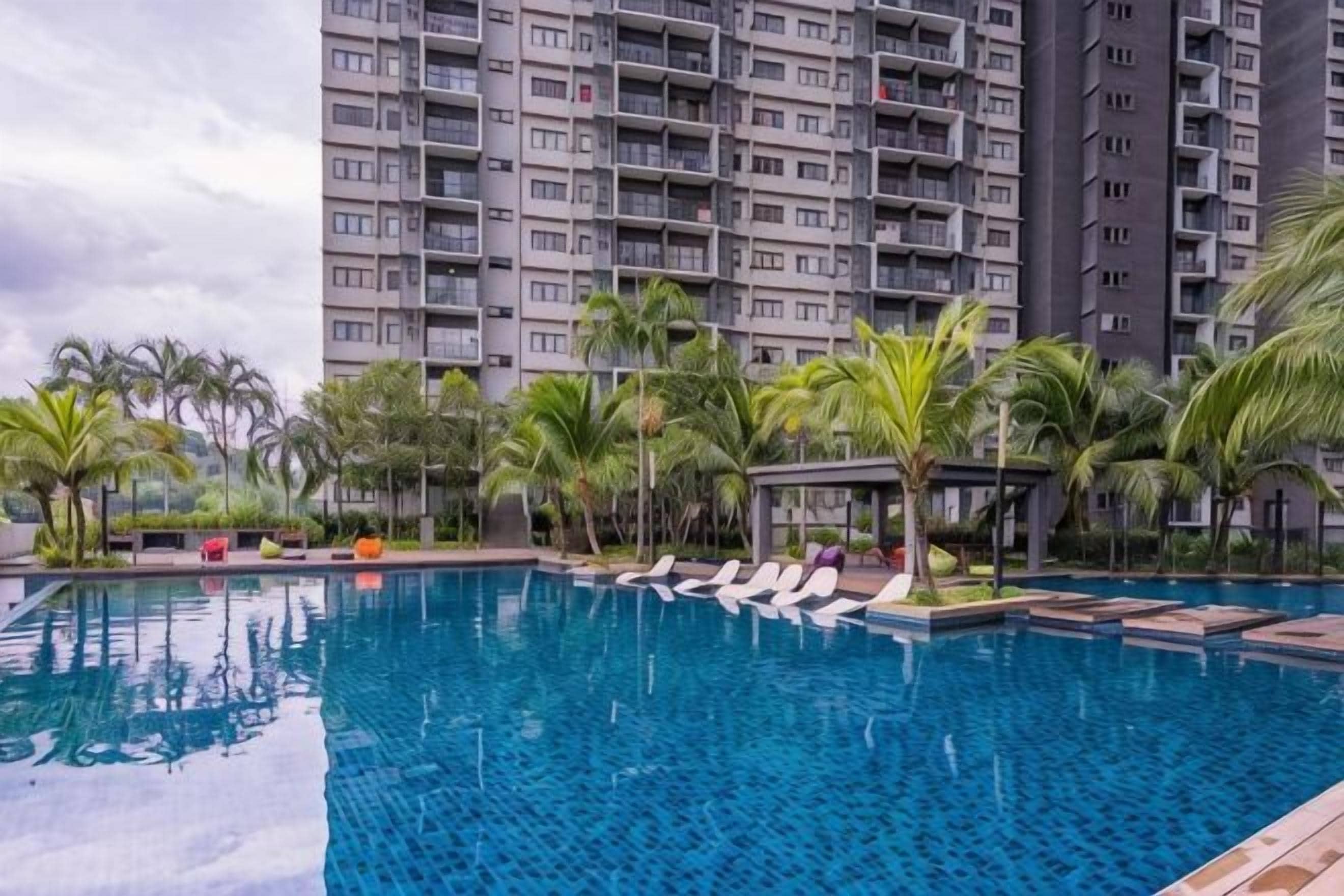 A swimming pool with lounge chairs, palm trees, and a high-rise building in the background.