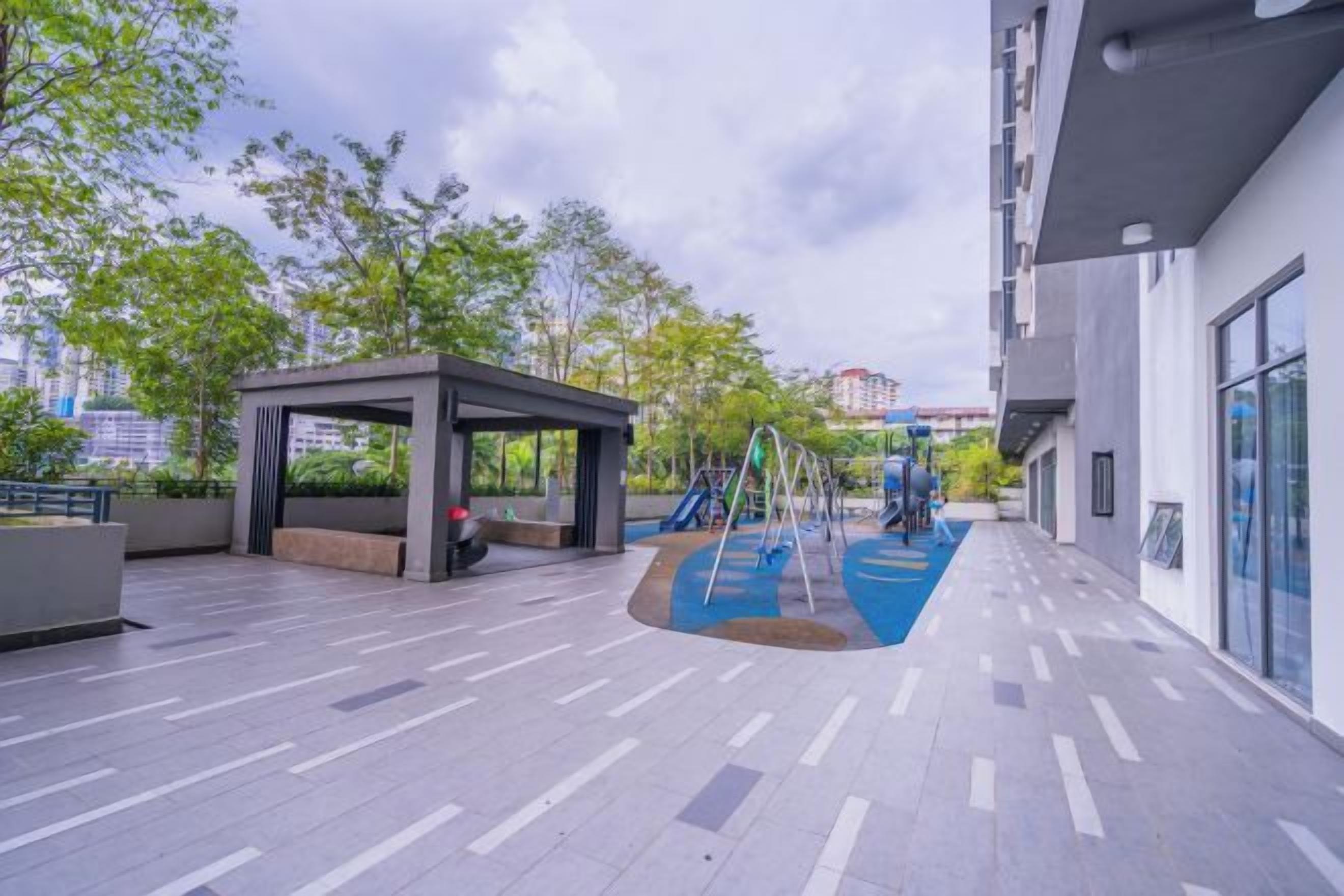 Un espacio al aire libre con zona de estar techada, juegos infantiles y un camino pavimentado.