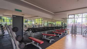Uma academia com equipamentos de musculação, bancos e um espelho grande.
