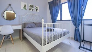 Een slaapkamer met een bed met wit metalen frame, een bureau met stoel, een spiegel en blauwe gordijnen.