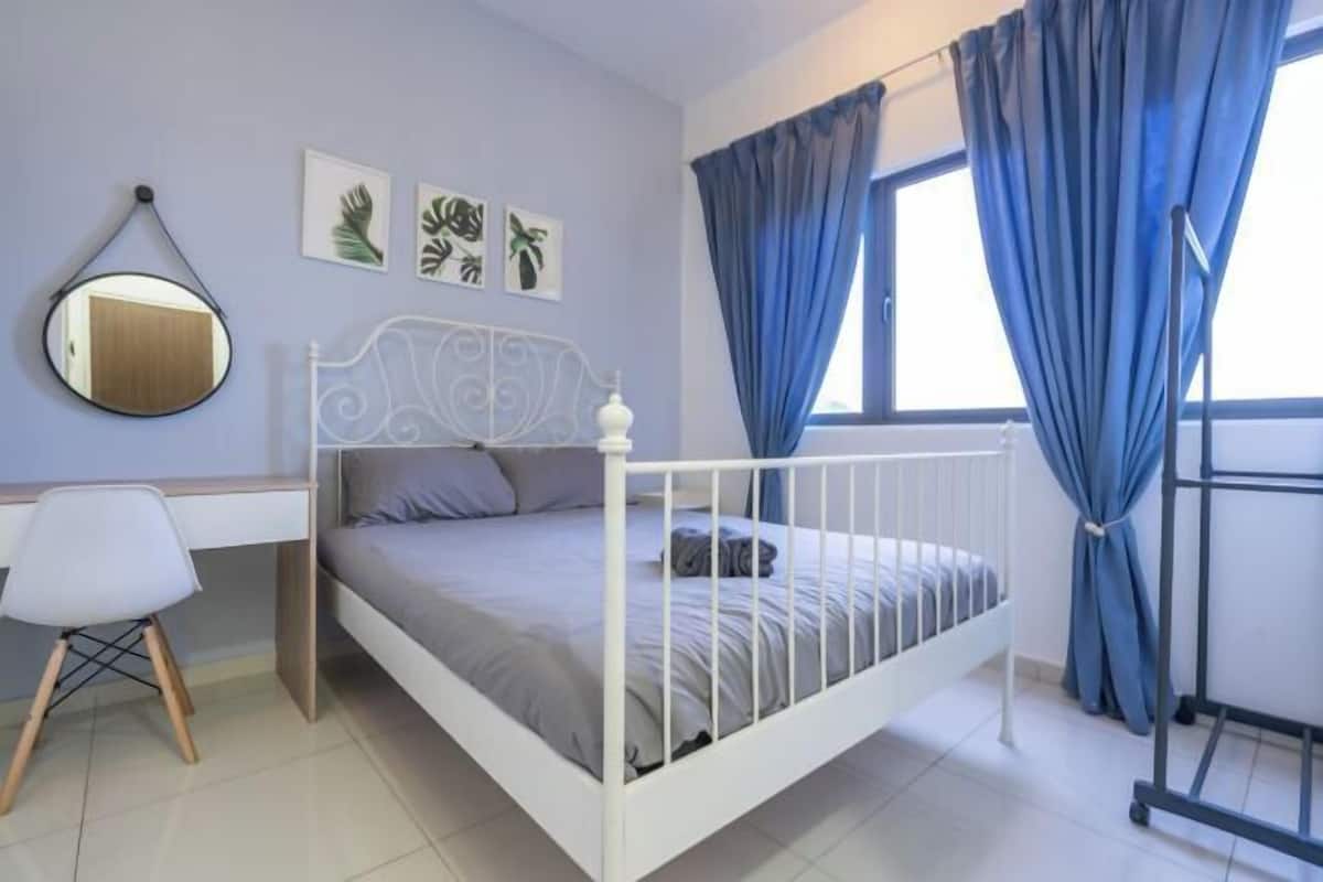 Un dormitorio con estructura de cama metálica blanca, un escritorio con silla, un espejo y cortinas azules.