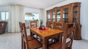 Een eetgedeelte met een houten tafel en stoelen, een grote houten kast en uitzicht door een raam met gordijnen.